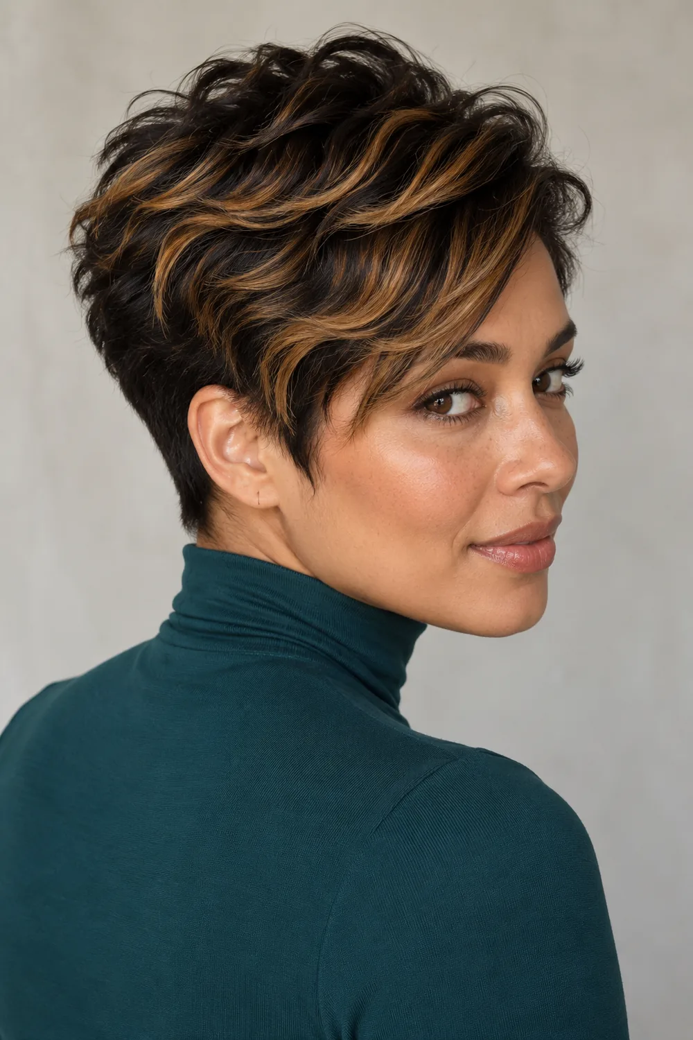 Adult woman in a teal high-neck top, wearing a textured black pixie with caramel highlights through its longer top layers.