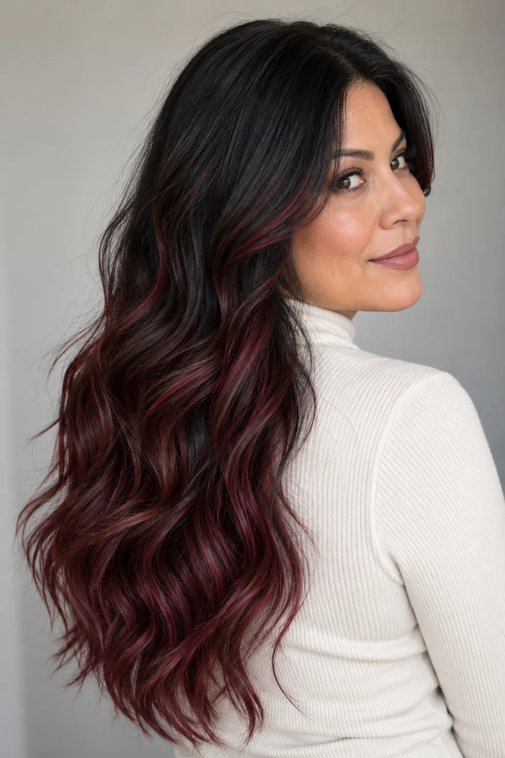 Adult woman in a cream high-neck top with long wavy black hair and burgundy highlights through the lengths and ends.