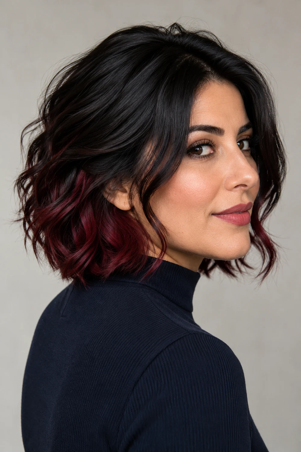 Three-quarter portrait of an adult woman with a black wavy bob and deep burgundy peekaboo underlayer visible at the nape and lower sides.