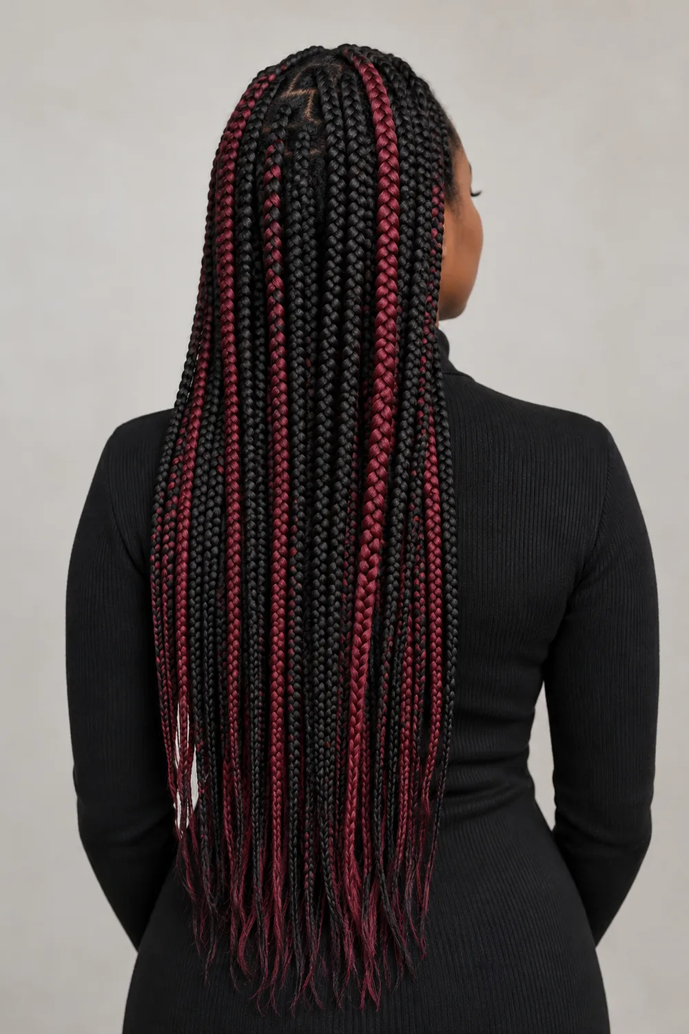 Rear three-quarter view of long black box braids with scattered burgundy braids from crown to ends, worn with a black high-neck top.