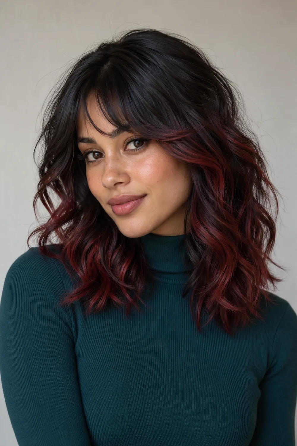 Adult woman with medium-length black waves, a mostly black curved fringe, and burgundy highlights through face-framing pieces and lower layers.
