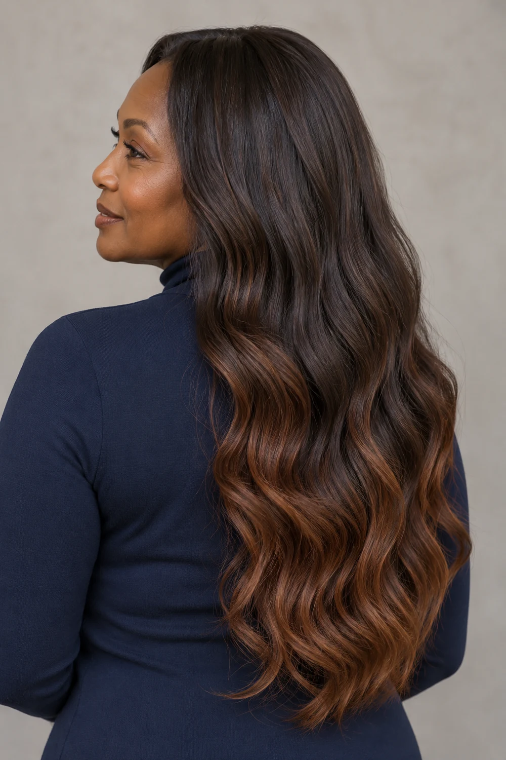 A woman in a navy high-neck top with long, dark brunette waves and soft cinnamon brown warmth concentrated through the lower lengths and ends.
