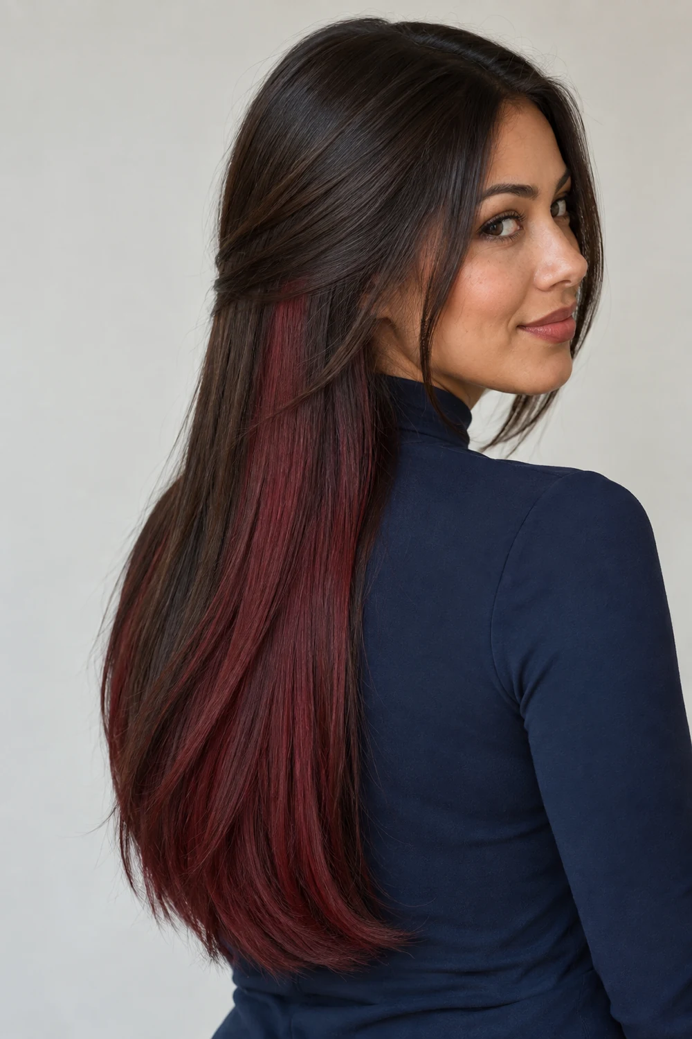 Adult woman in a navy high-neck blouse, showing long dark brown hair with a broad burgundy underlayer panel from a three-quarter angle.
