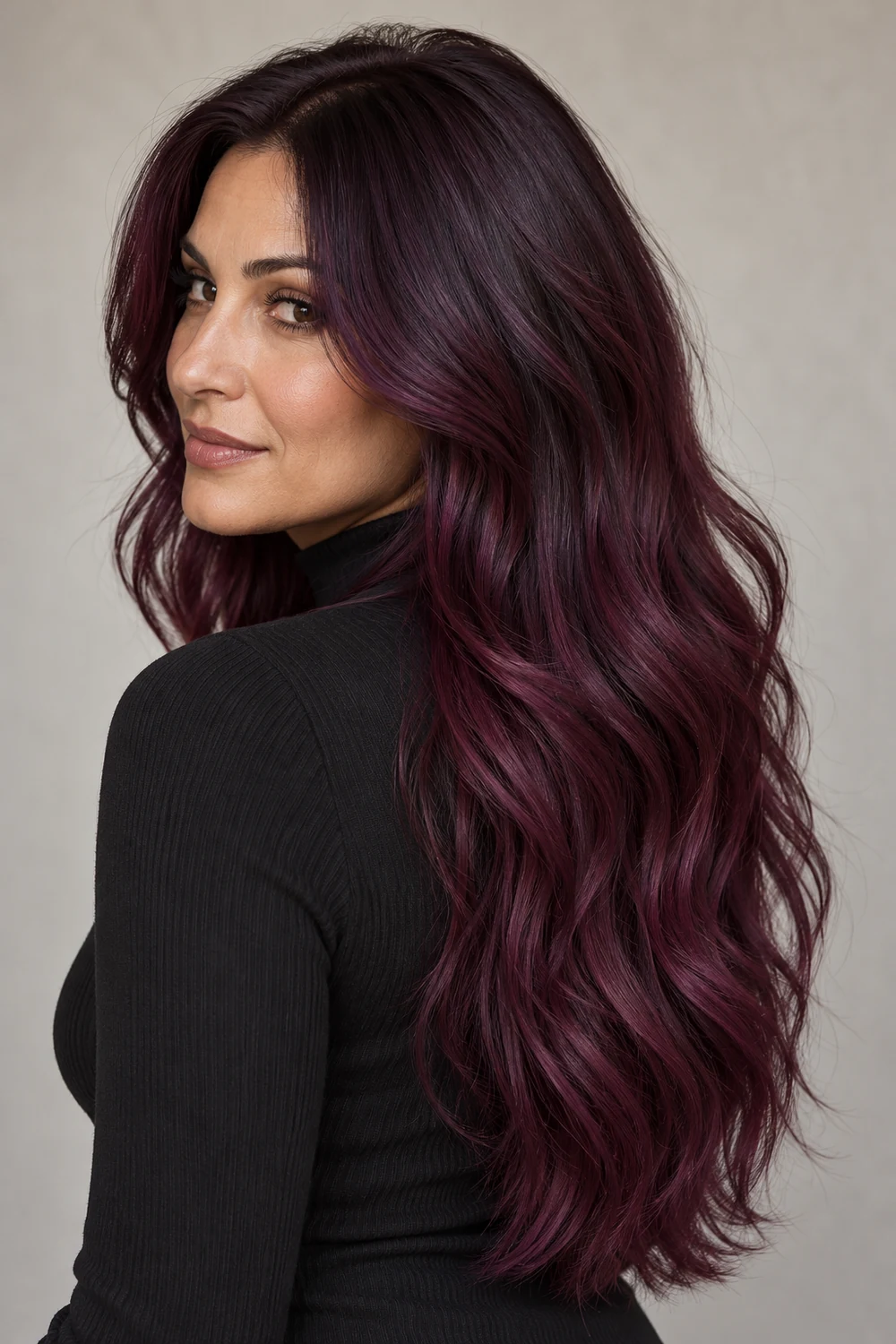 Long, layered plum waves transition from near-black aubergine roots to brighter red-violet lengths and ends, shown over one shoulder.