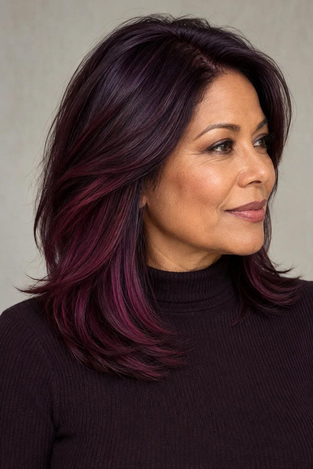 A woman with shoulder-length layered deep plum hair and broad red-violet panels, wearing a dark high-neck top against a neutral background.