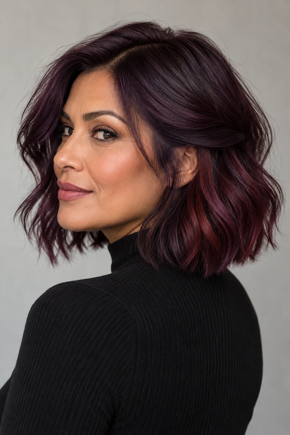 A woman with a collarbone-length deep plum bob, showing warm burgundy-violet color beneath the side and lower layers.