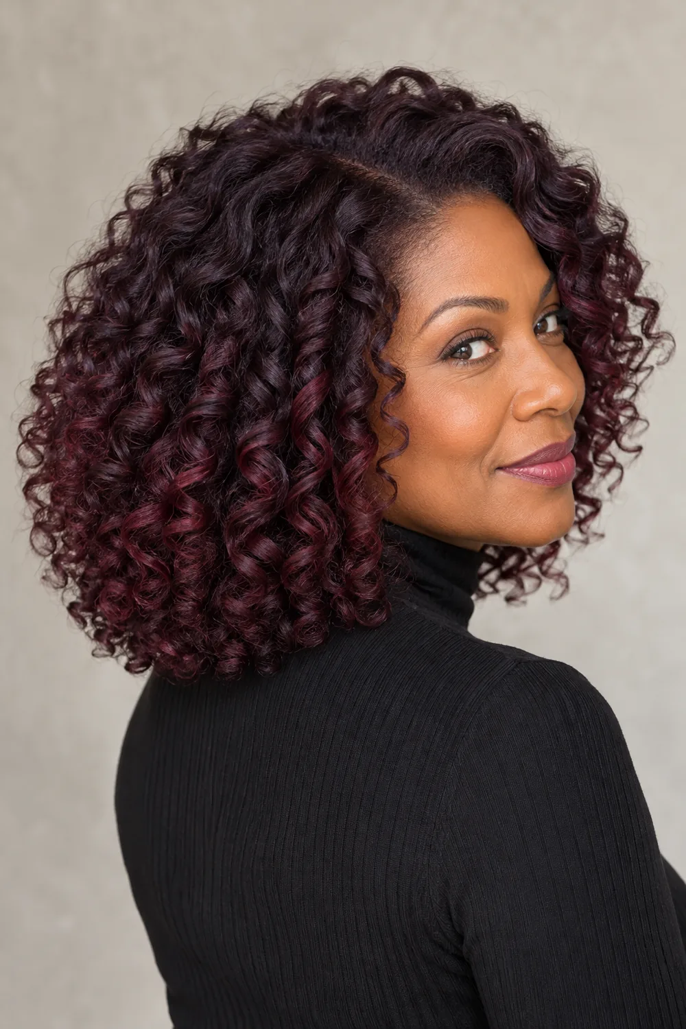 Adult woman in a rear three-quarter portrait with shoulder-length dark plum curls and curved burgundy-violet accents.