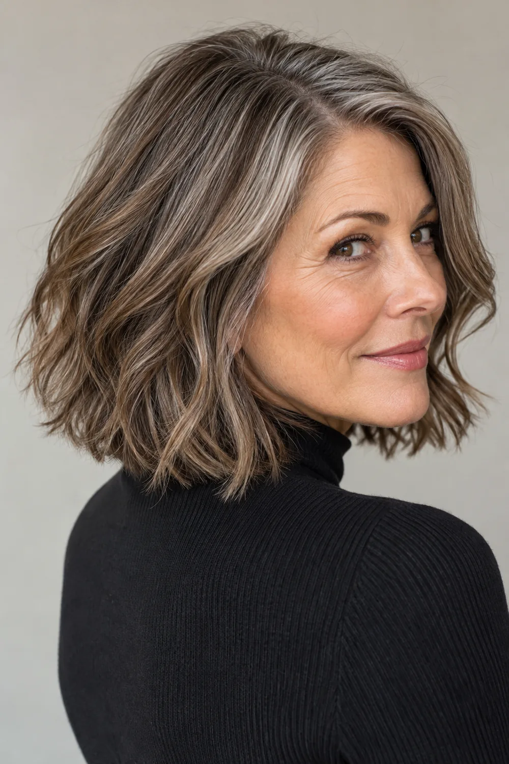 Mature woman in a rear three-quarter portrait with a shoulder-length brunette bob, visible silver strands, and muted brown lowlights.