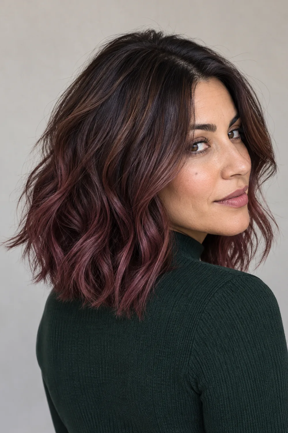 Woman with medium olive-cool skin and a shoulder-length brunette shag with plum balayage through the lengths and tips, photographed in three-quarter view.