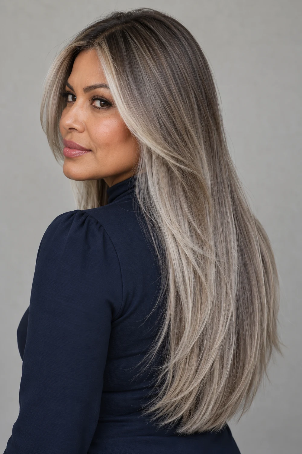 Long silver-beige ash-blonde layers with deeper roots, fine lowlights, and light face-framing pieces on a woman in a navy high-neck blouse.