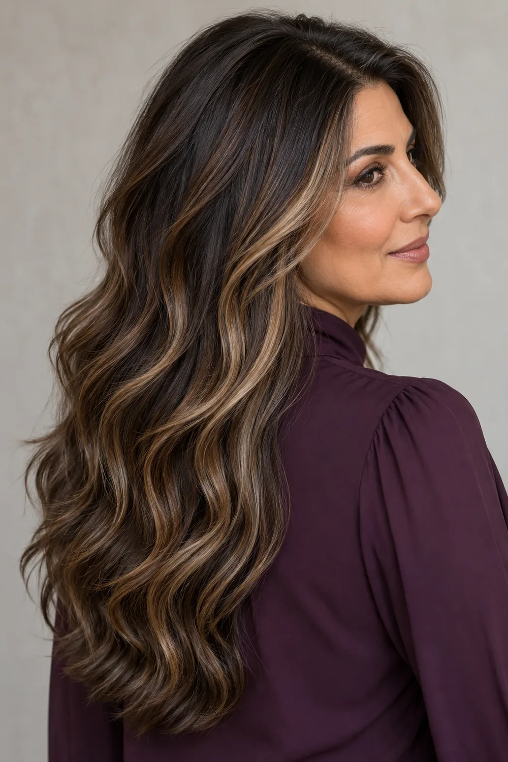 Long deep brunette waves with beige caramel ribbons from below the crown, shown on a woman in profile wearing a plum blouse.