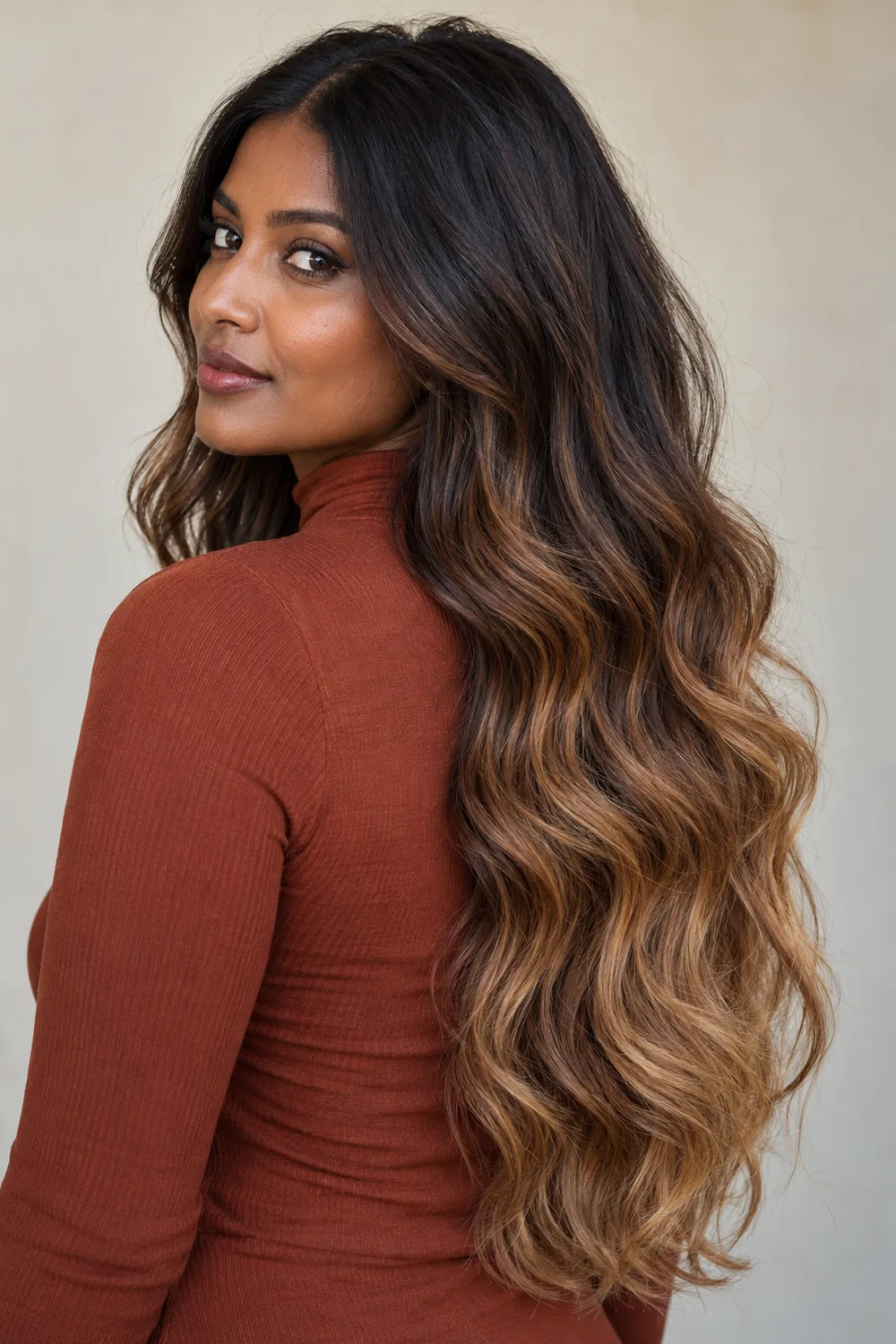 An adult Indian woman with deep skin and waist-length loose waves, transitioning from dark chocolate roots to caramel ends.
