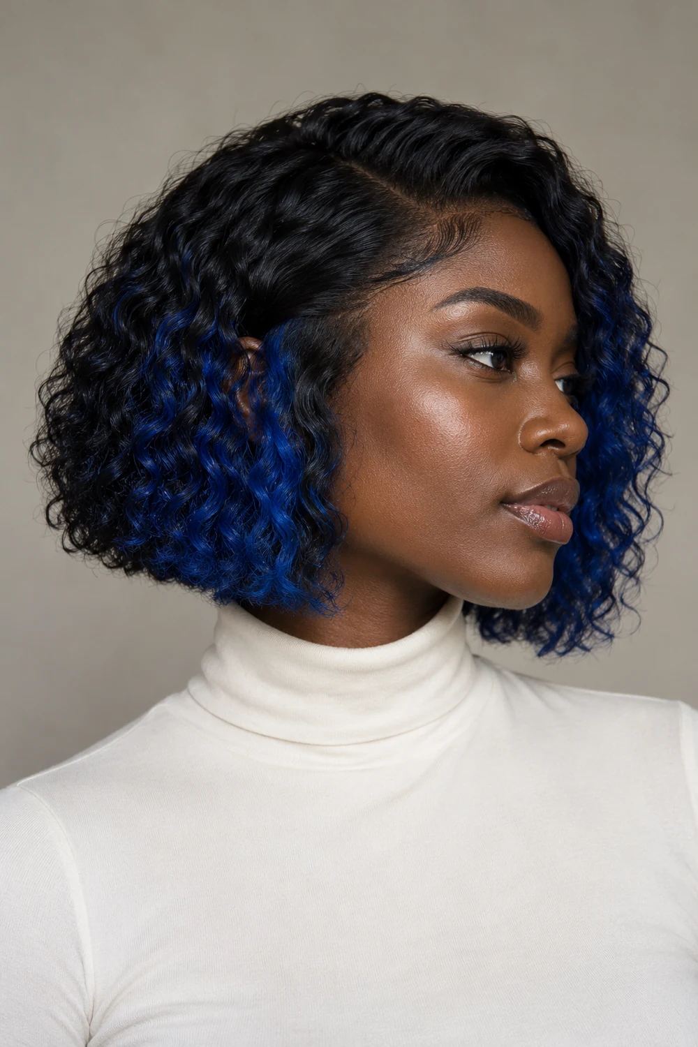Three-quarter portrait of an adult woman with deep warm-toned skin and a curly jaw-length blue-black bob, vivid cobalt color visible through the lower layers and around the front edges.