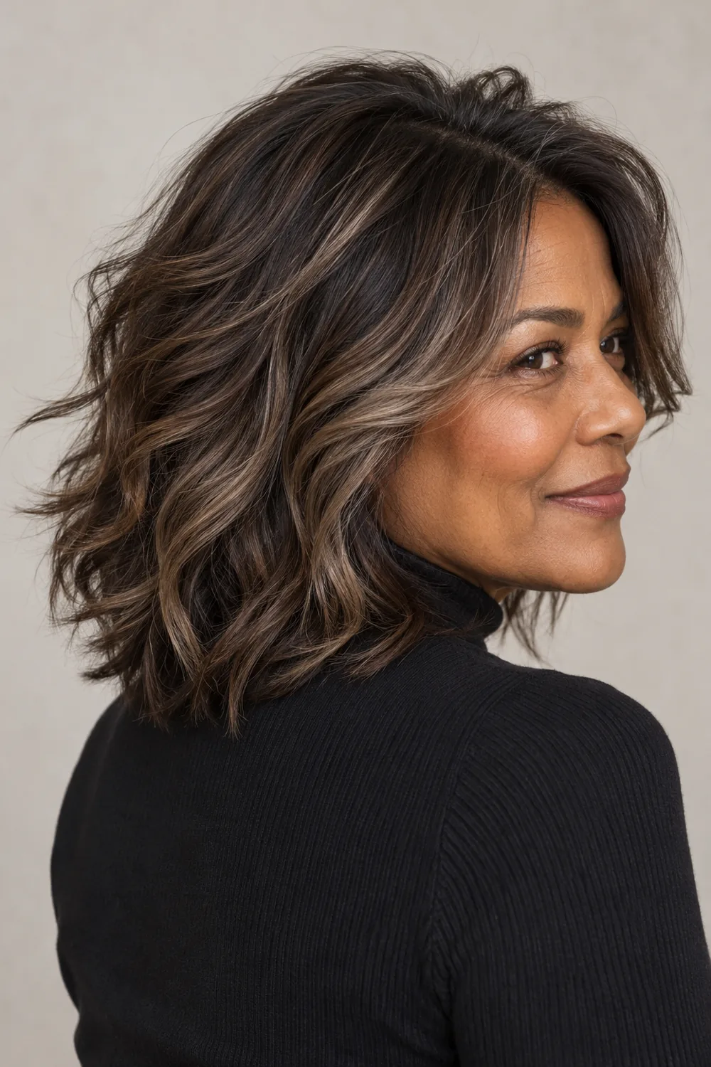 A woman with a shoulder-length wavy brown shag and smoky taupe ribbon highlights, shown from a rear three-quarter angle.