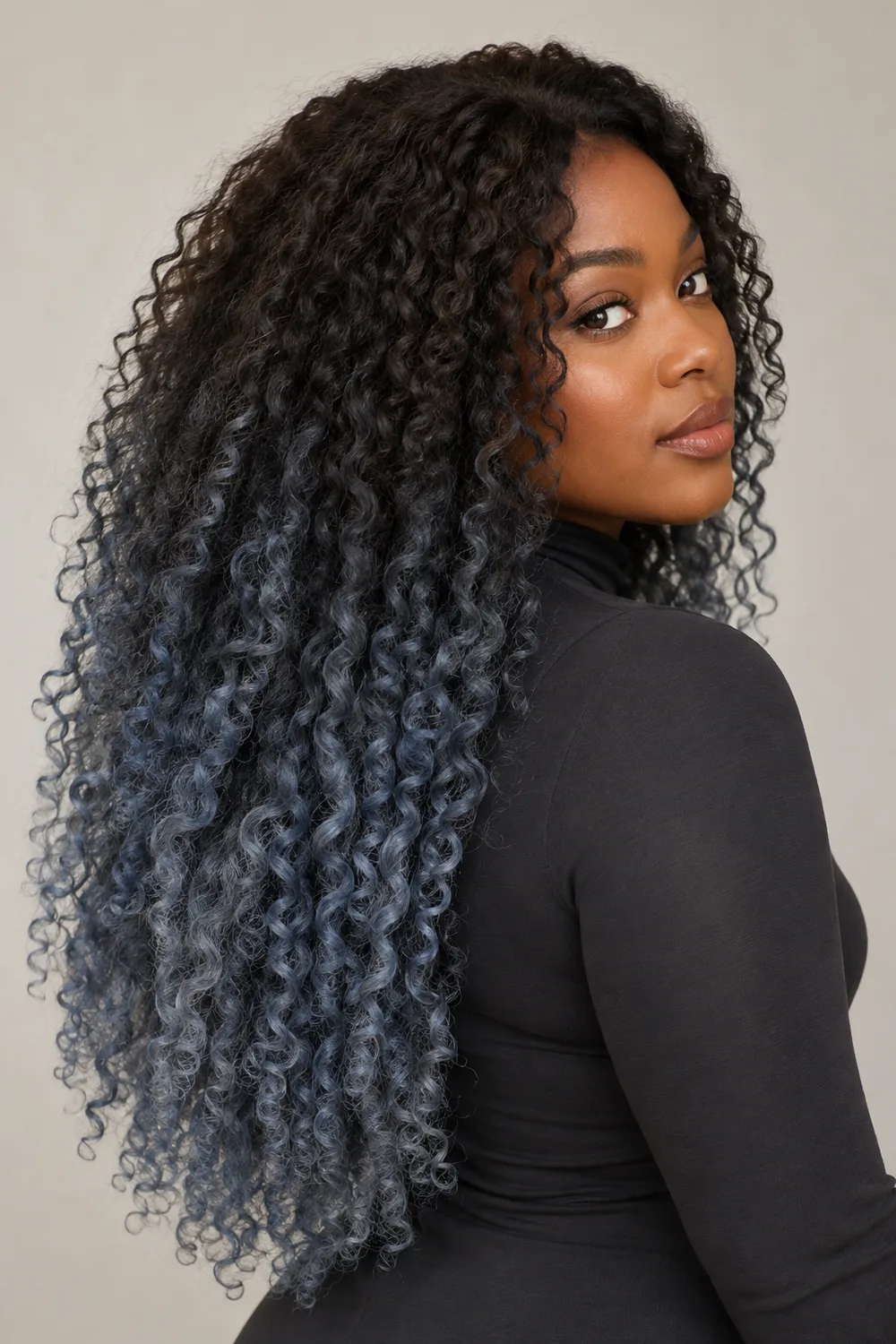 A woman with long dense curls, dark brown at the roots fading into muted smoky blue-gray through the lengths.
