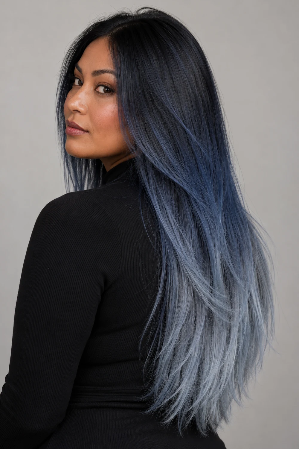 A woman in a black high-neck top with long straight hair transitioning from a blue-black crown through smoky blue to pale gray-blue tips.