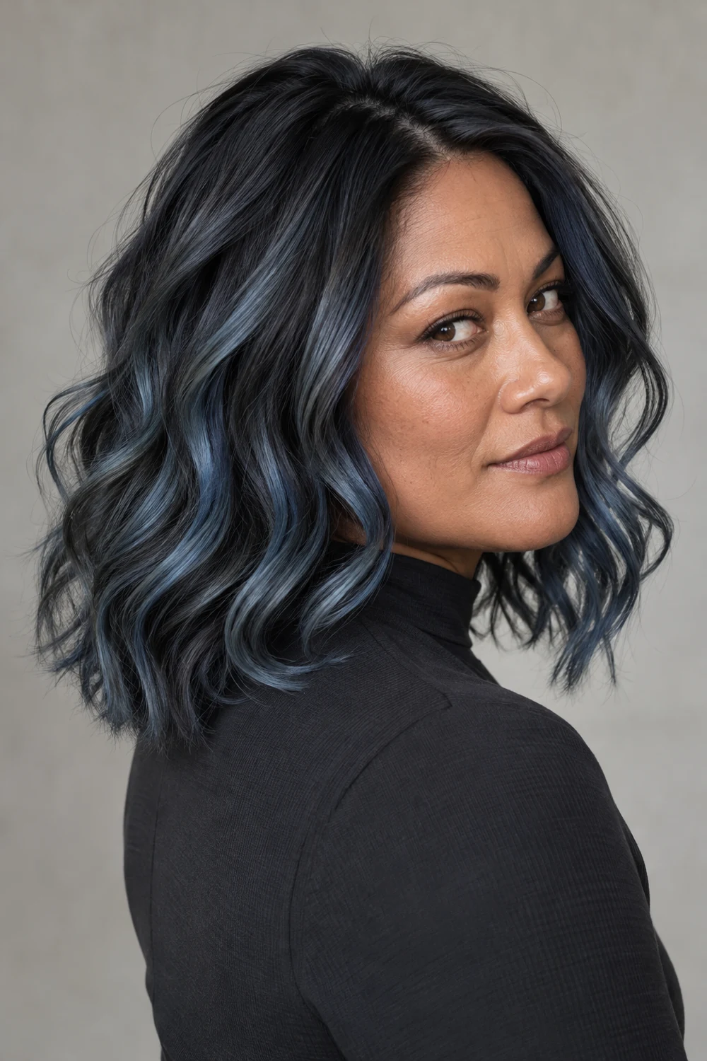 Adult woman in a charcoal high-neck top, showing shoulder-length dark waves with muted smoky blue and gray ribbons from a rear three-quarter angle.