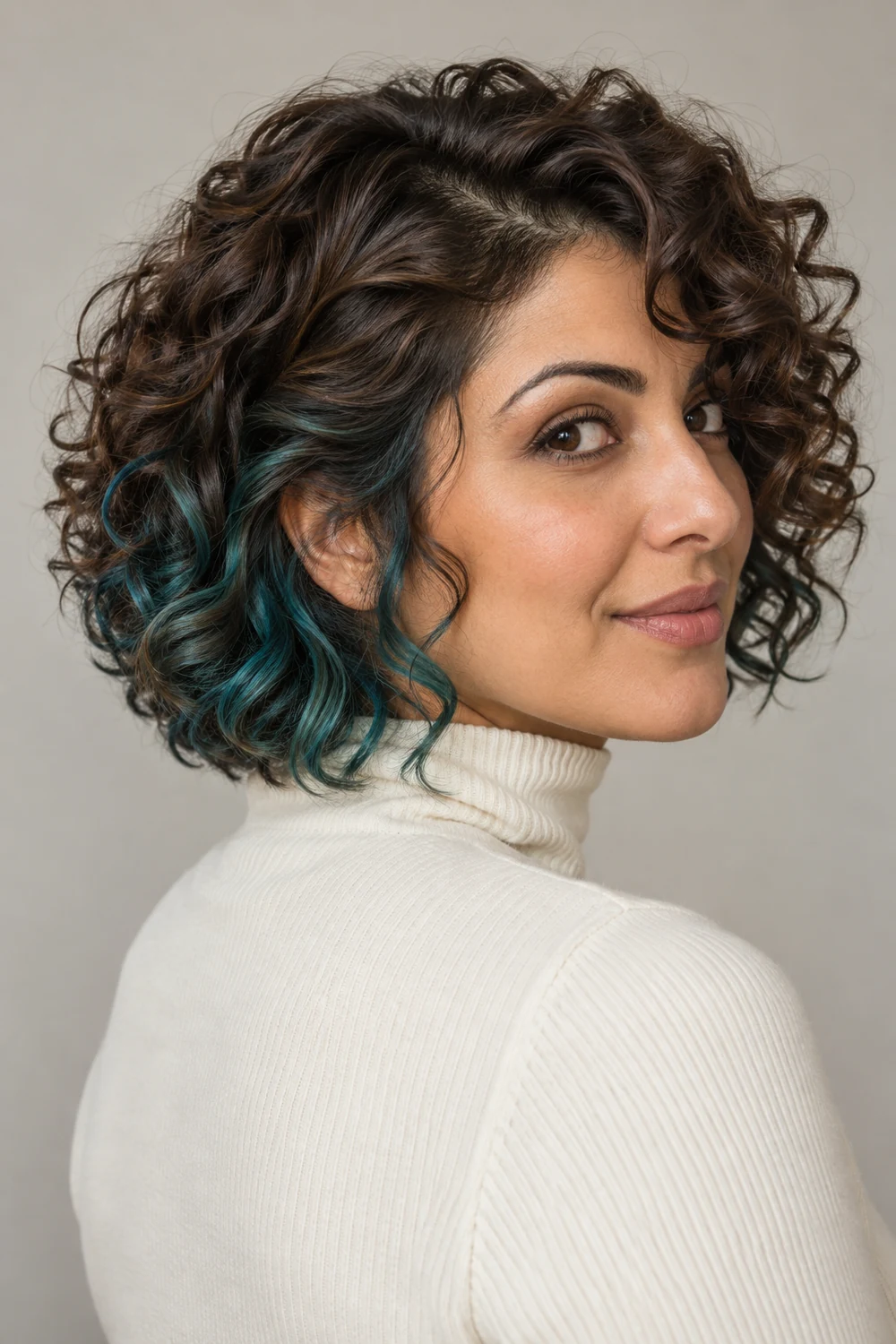A woman with a chestnut curly bob turned slightly to reveal blue teal underlayer curls near the side and nape.
