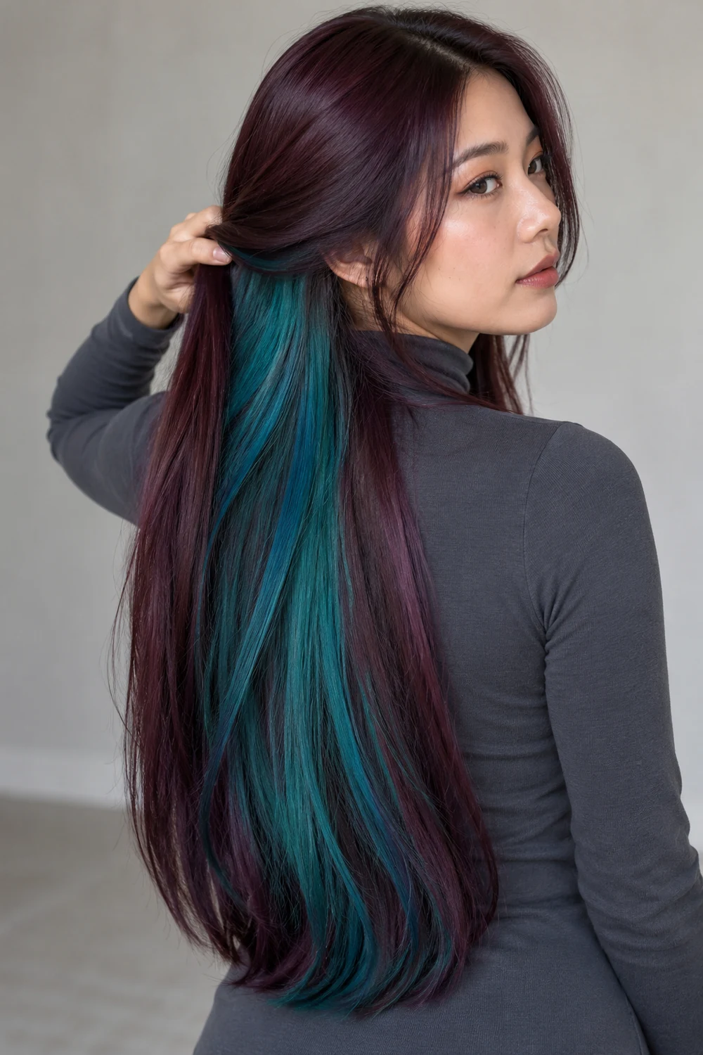 Adult woman with waist-length straight plum hair swept aside to reveal a broad turquoise-teal underlayer.