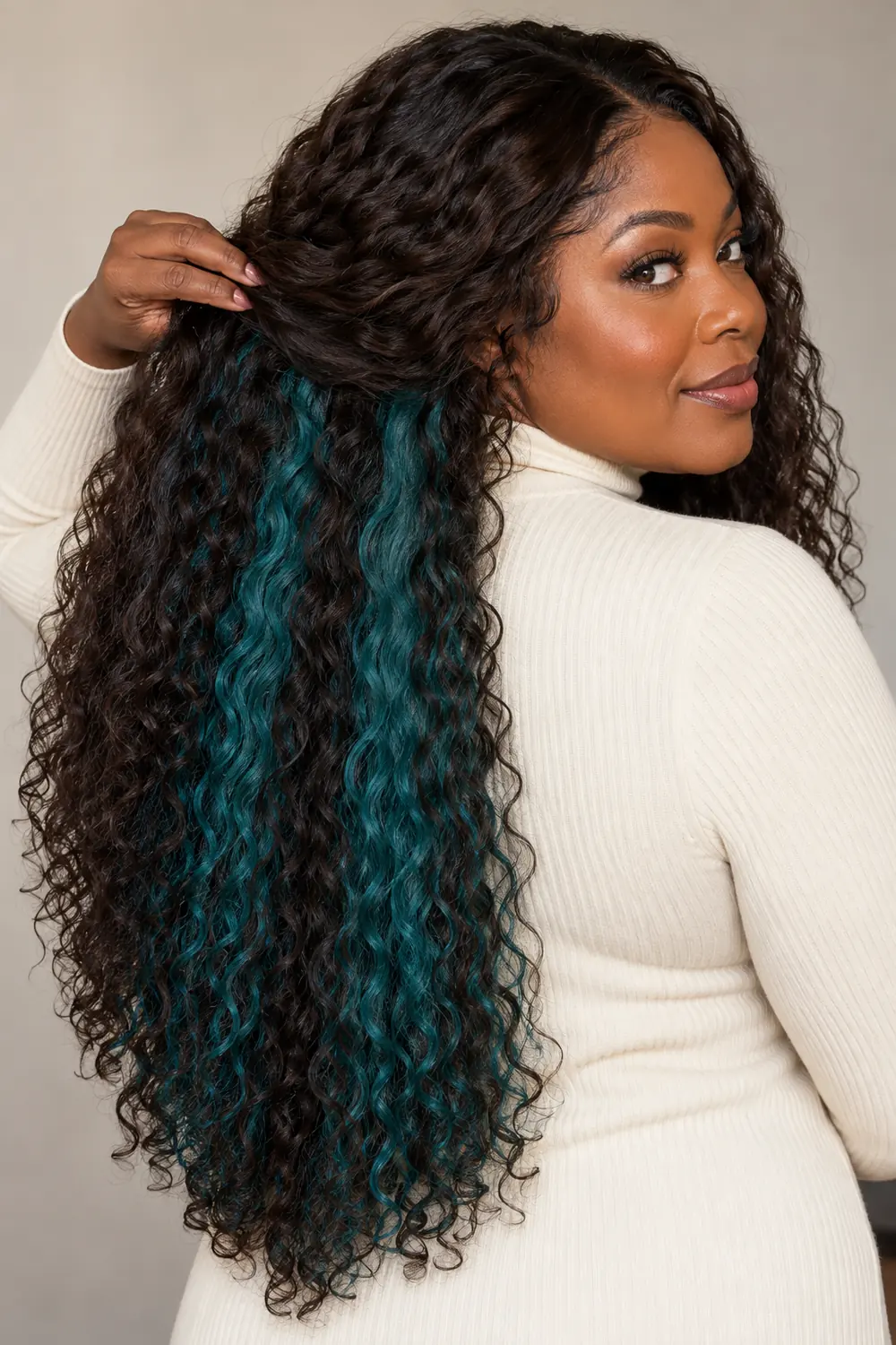 A Black woman in a cream high-neck top lifts the dark chocolate outer layer of her long hair to reveal two blue-teal underlayer panels.