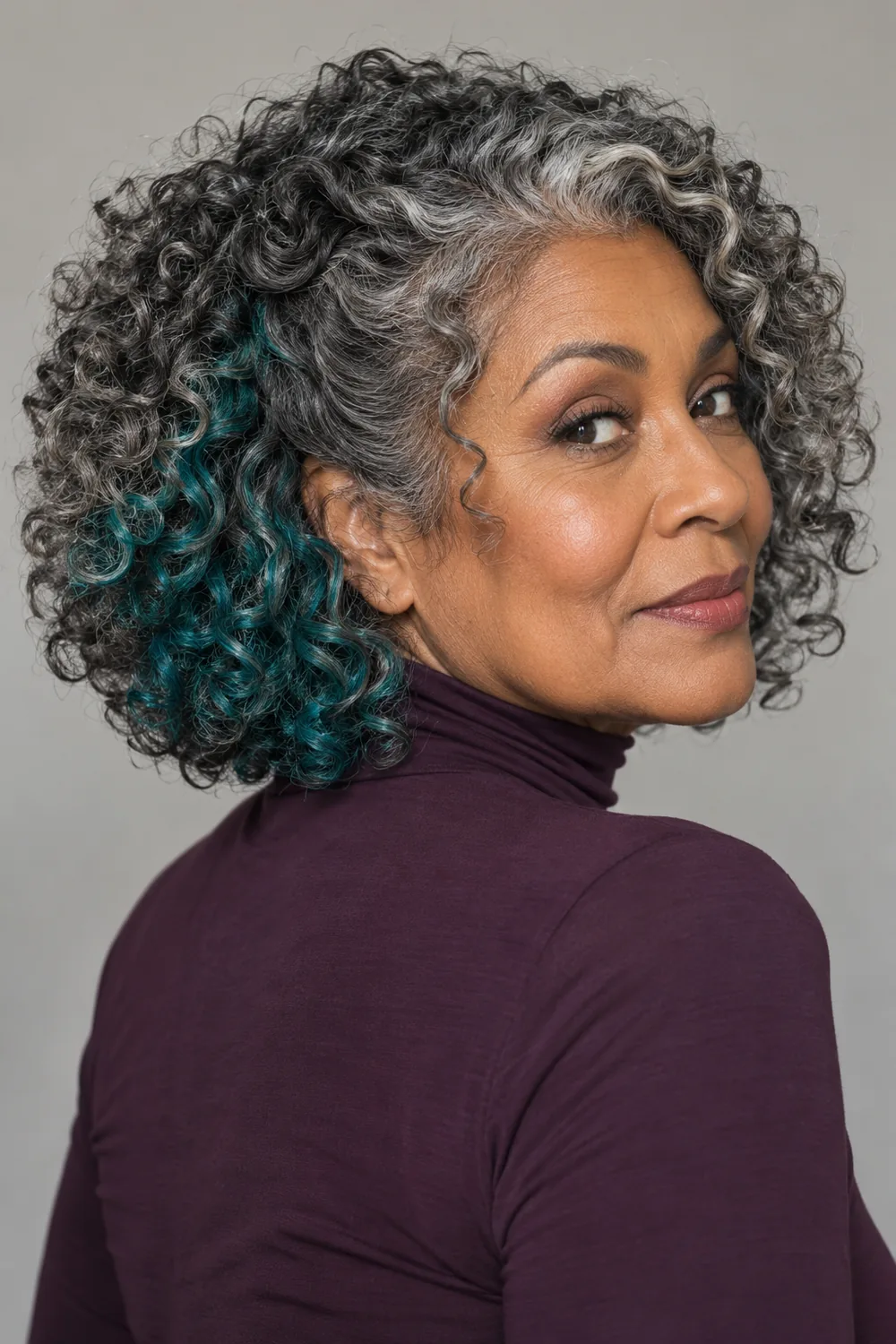 Adult woman in a three-quarter pose with rounded salt-and-pepper curls and a visible teal underlayer through the lower side curls.