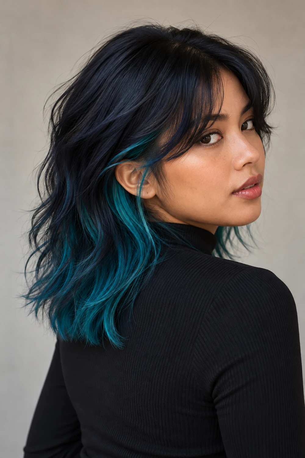 Adult woman in a three-quarter portrait with a midnight-blue layered wolf cut, vivid teal visible beneath the back layers and beside the temple.
